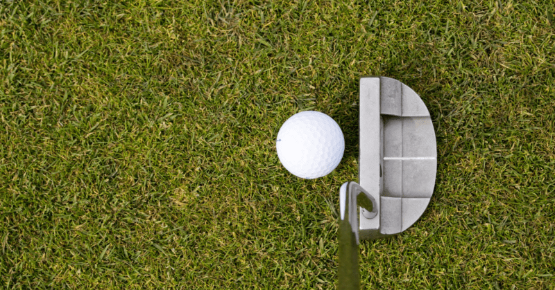 A zoomed in photo of a putter about to hit a golf ball.