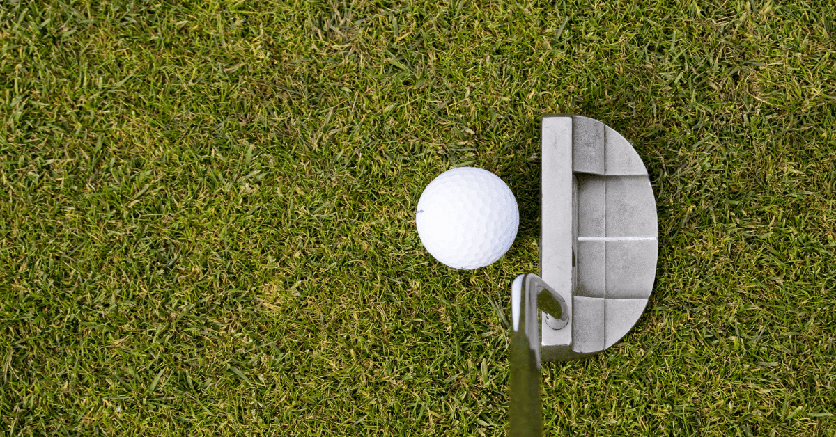 A zoomed in photo of a putter about to hit a golf ball.