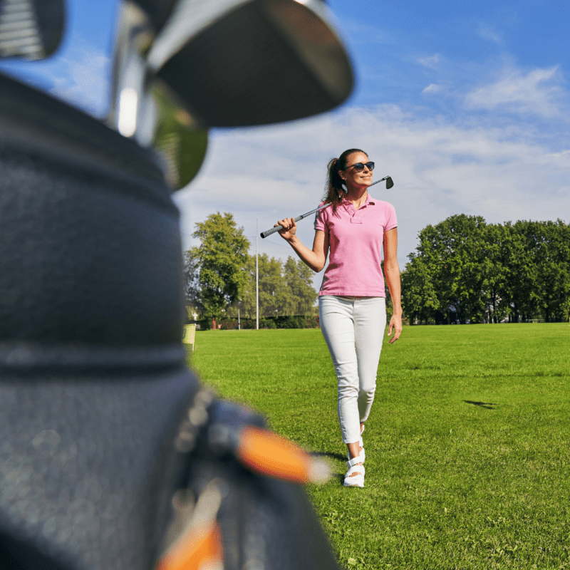 A woman with a golf club walking towards a golf bag.