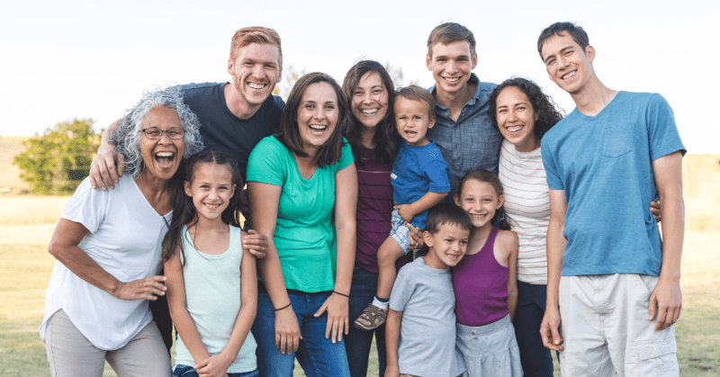A family of 11 people smiles and poses for a picture. They are all different ages.